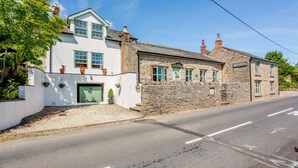 A two-story stone building with a white facade, a green door, and a small porch with potted plants. - Broadrock (Chepstow)