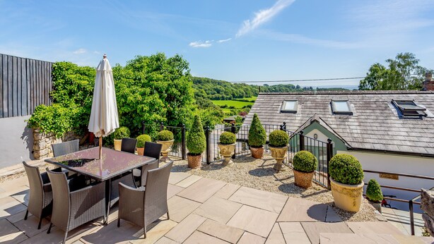 A patio with a table and chairs, surrounded by potted plants and a view of the countryside. - Broadrock (Chepstow)