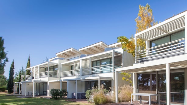A modern multi-story hotel with balconies, large windows, and a well-maintained lawn. - Troia Residence Beach Houses (Grandola)