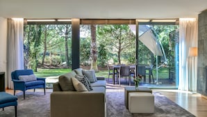 A modern living room with a large sliding glass door leading to a patio with a dining table and chairs. - Troia Residence Beach Houses (Grandola)