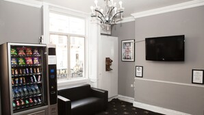 Habitació amb màquina expenedora, sofà de cuir negre, televisió de pantalla plana i quadres a la paret.