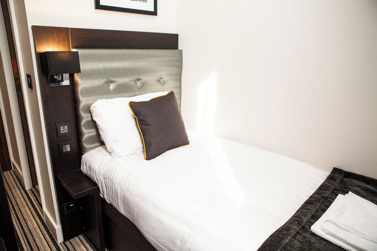 A neatly made bed with a headboard, a bedside table, and a wall-mounted light fixture.