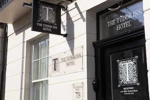 The exterior of The Tudor Inn Hotel with a prominent 'T' sign and a reception sign indicating the location at the Blair Victoria Hotel.
