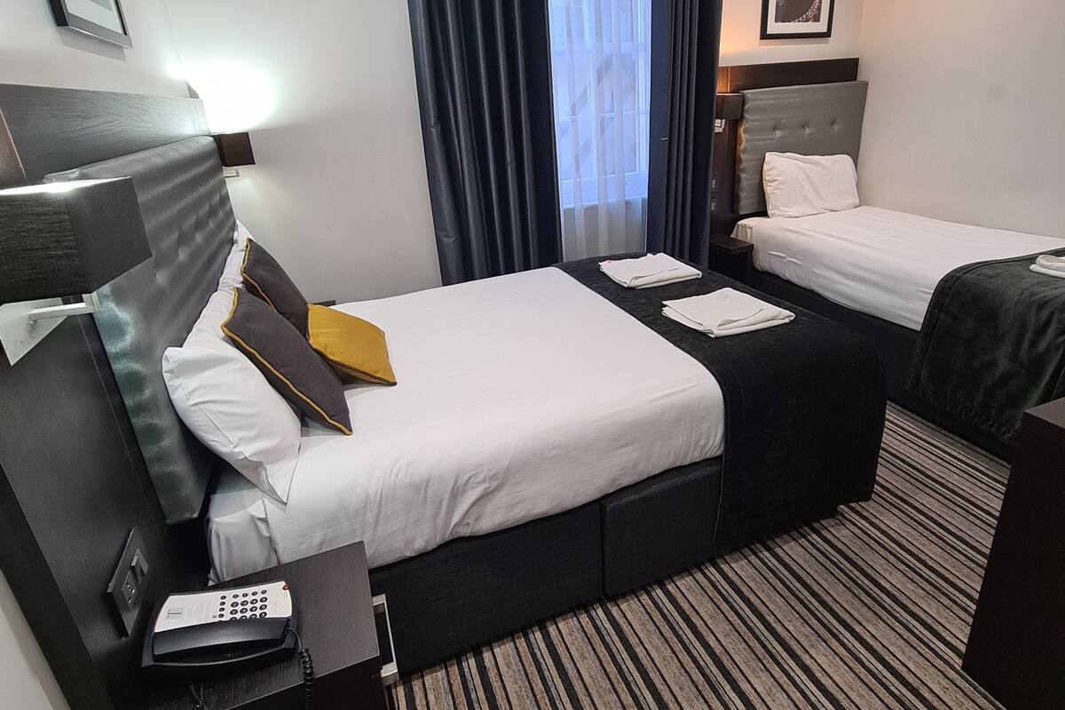 A hotel room with two beds, a desk with a telephone, and a striped carpet.