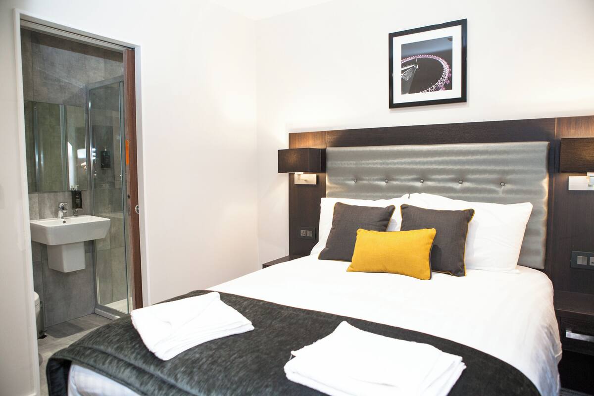A hotel room with a bed, a bathroom with a glass shower enclosure, and a framed picture on the wall.