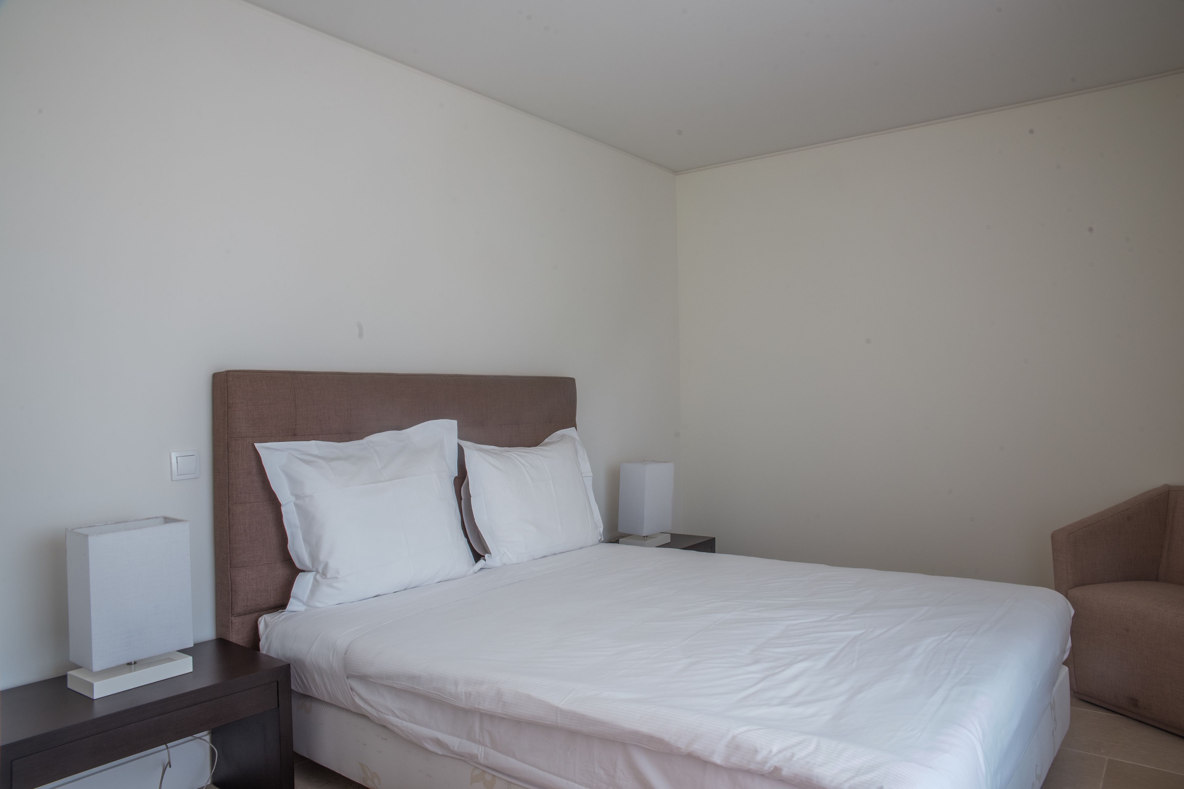 A neatly made bed with white linens, a wooden headboard, and two bedside tables with lamps.