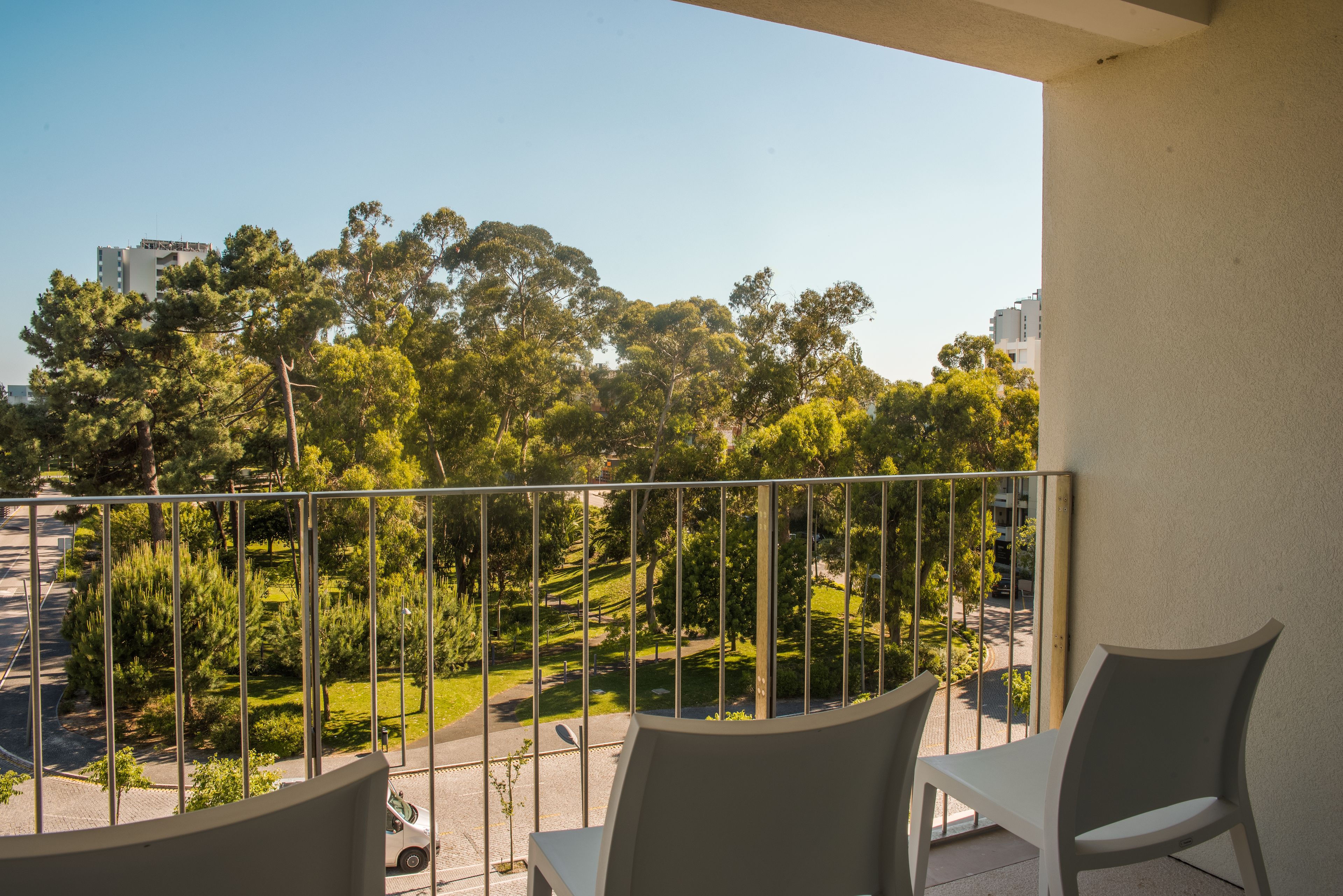 A balcony with two chairs, a view of a park with trees and a building in the background.
