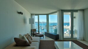 Une chambre d’hôtel moderne dotée d’un grand balcon, d’un canapé, d’une table basse et offrant une vue sur la mer et les bateaux.