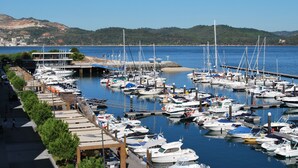 Un port de plaisance où sont amarrés de nombreux bateaux, une promenade piétonne et, en arrière-plan, des collines.