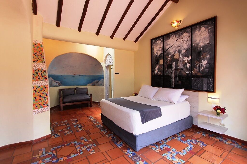 A bedroom with a bed, a nightstand, a wall-mounted painting, and a tiled floor.
