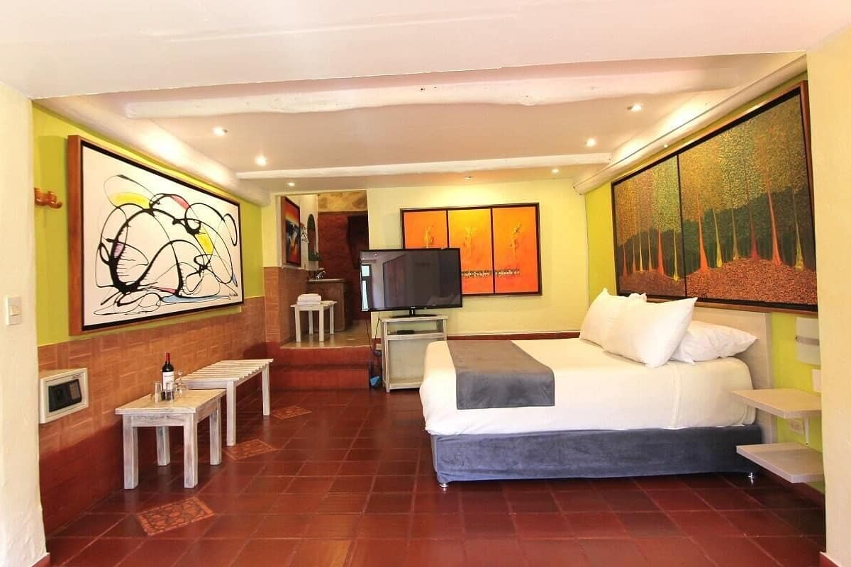 Una habitación de hotel con una cama, televisión, una mesita y obras de arte en las paredes.