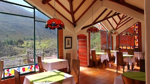 A restaurant with tables set for dining, large windows with a view of a mountainous landscape, and colorful stained glass windows. - Suites Arcoiris (Villa de Leyva)