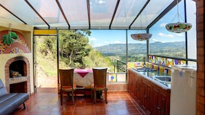 A patio with a table and chairs, a brick oven, and a view of the countryside. - Suites Arcoiris (Villa de Leyva)