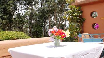 Una mesa con mantel blanco, un florero con flores y una silla azul.