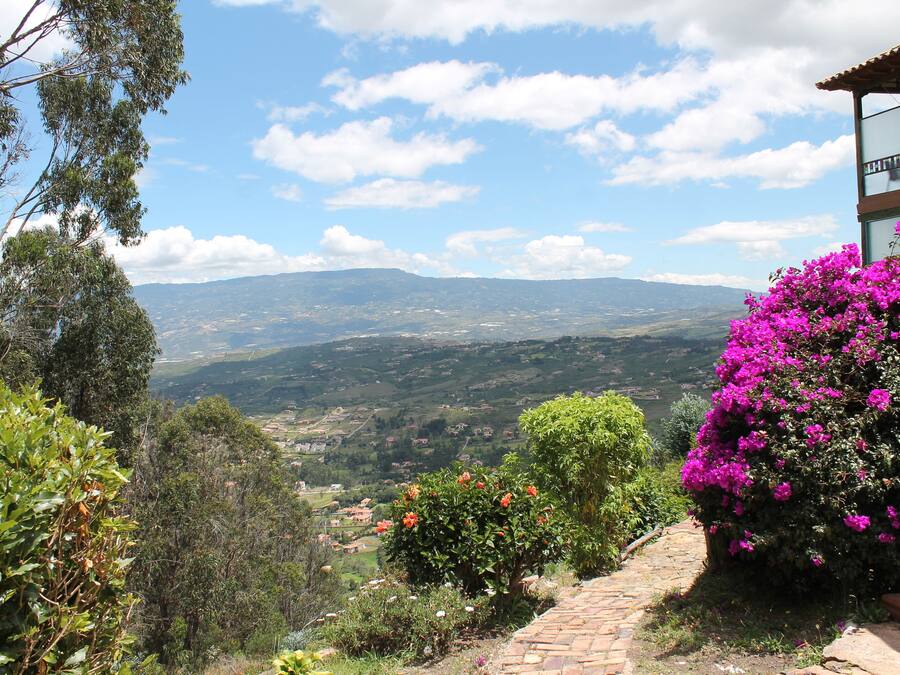 A hillside view with a stone pathway leading to a building with a balcony overlooking a valley.