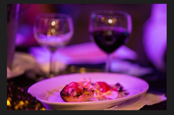 Un plato de comida con una copa de vino tinto al fondo.