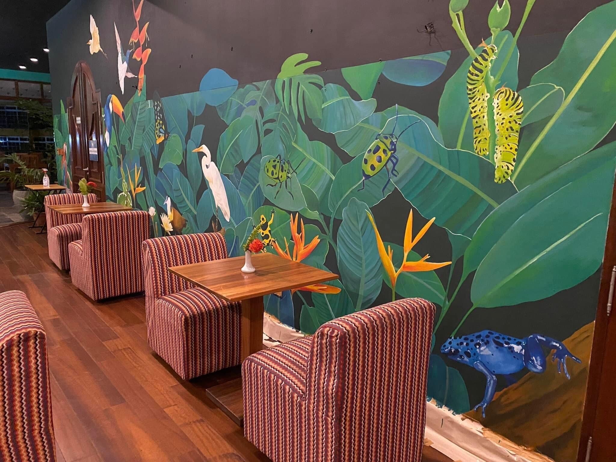 A restaurant with striped cushioned seating, a mural of tropical foliage and wildlife, and a wooden floor.