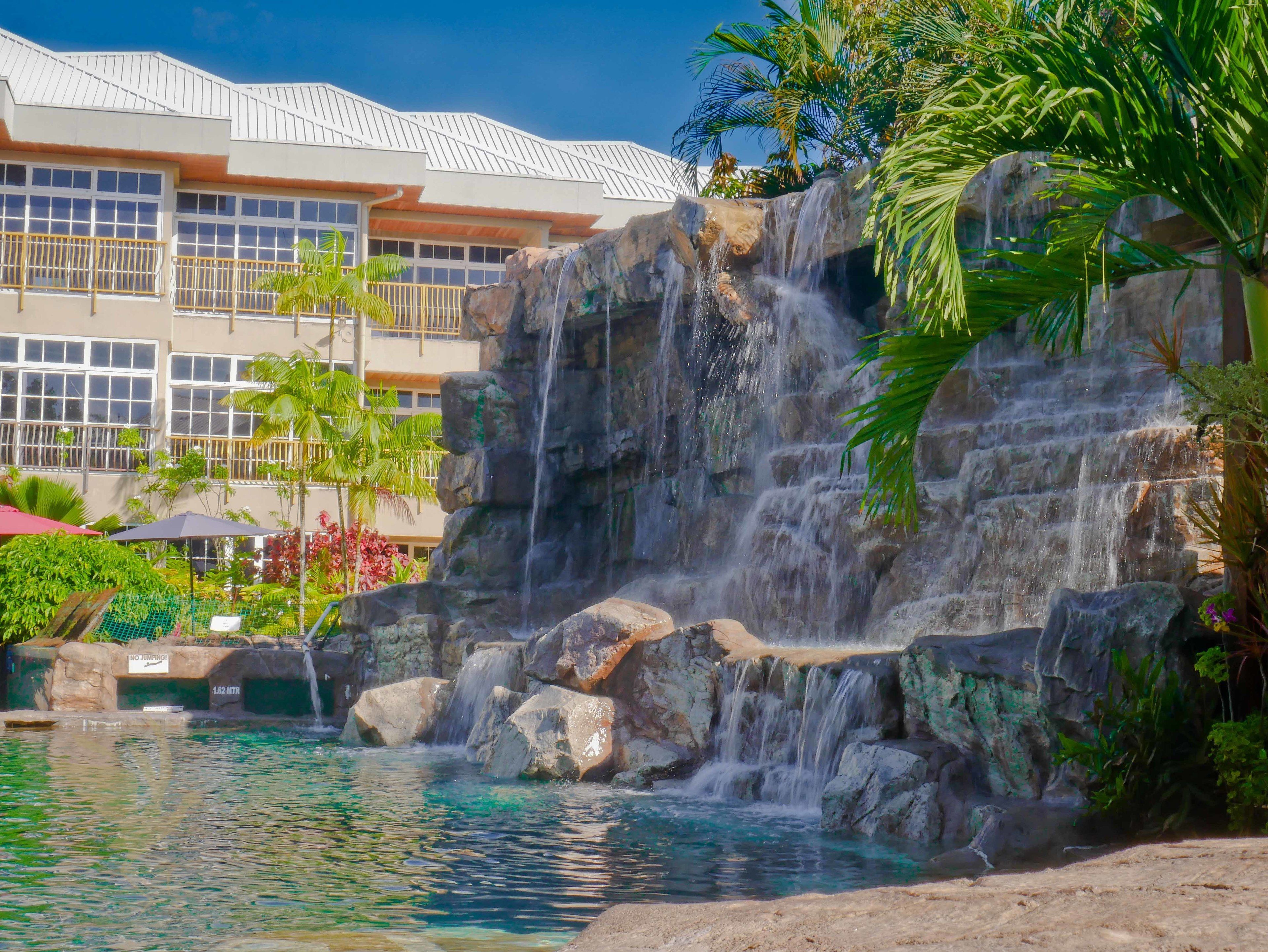 Um hotel com uma cascata, piscina e um edifício com varandas.