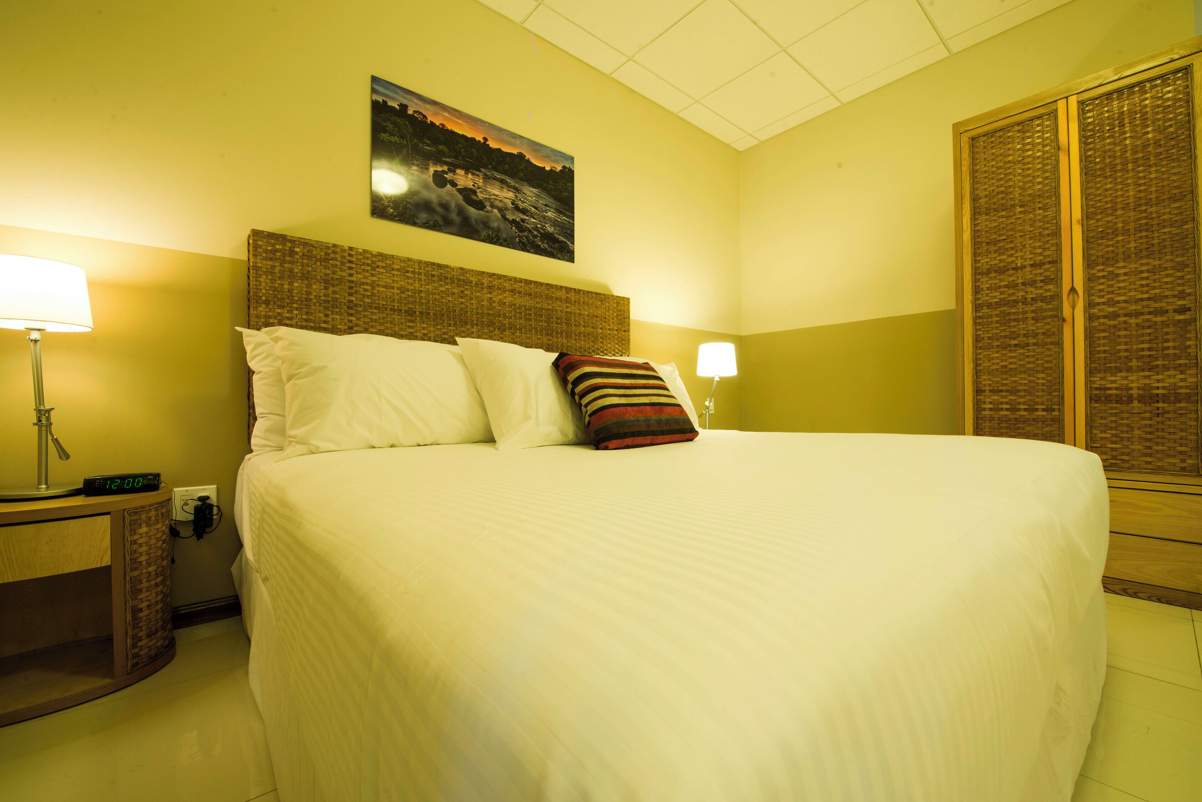 Una habitación de hotel con una cama grande, una mesita de noche, una lámpara, un reloj de pared y un cuadro.
