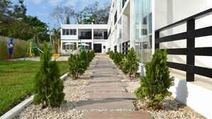 A pathway leading to a building with a modern design, a playground, and small trees along the path. - Ocean Blue Hotel (Manglaralto)