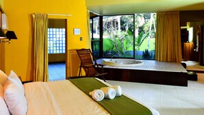 Une chambre d’hôtel comprenant un lit, un coin salon avec vue sur la verdure, une fenêtre avec des rideaux et une salle de bain avec baignoire.