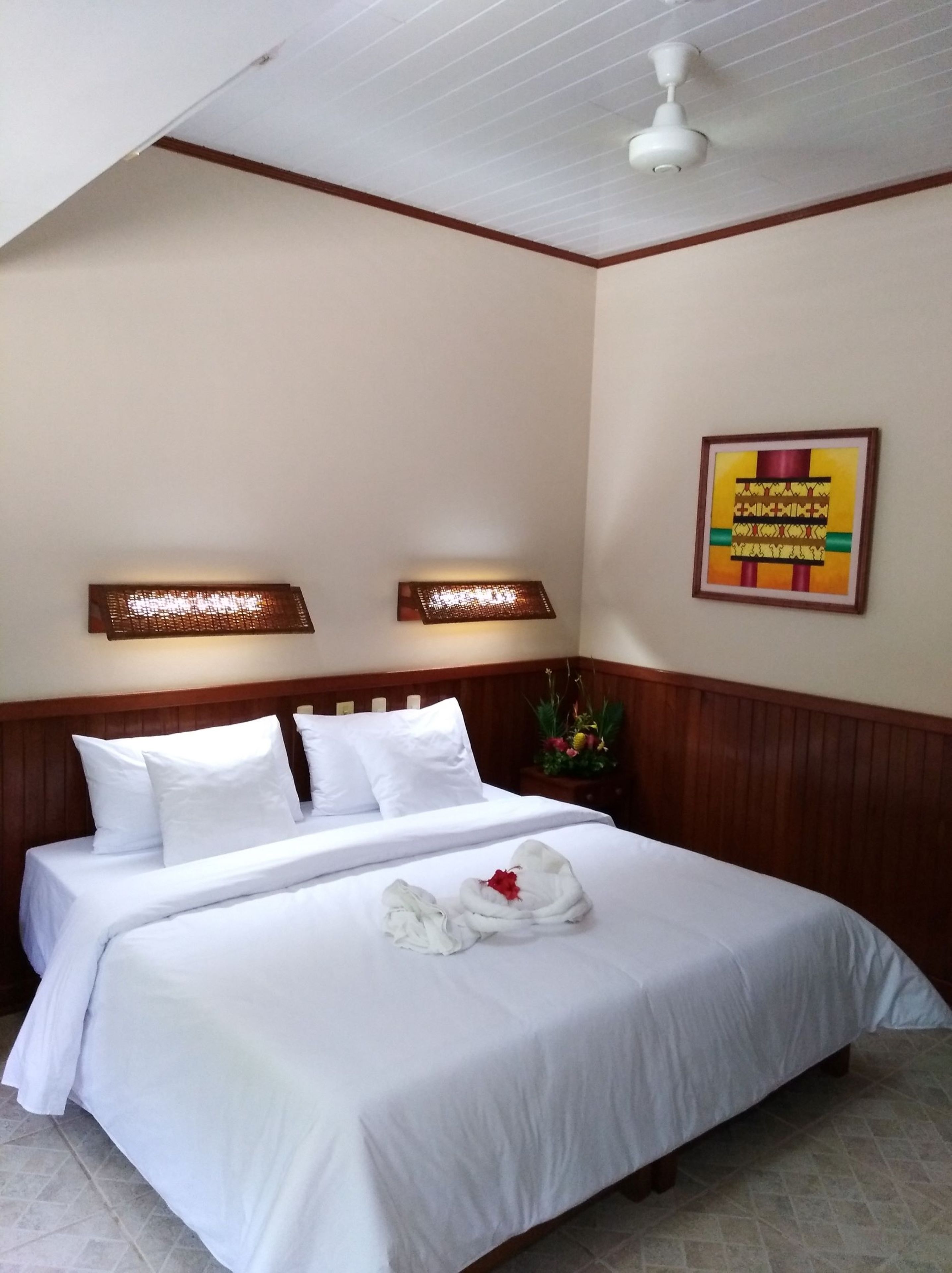 A neatly made bed with white linens, a wooden headboard, and a framed picture on the wall.