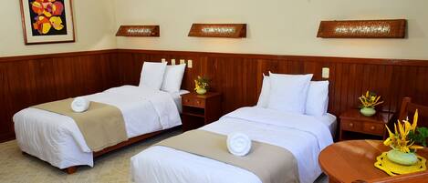 Two single beds with white linens and beige bedspreads, wooden headboards, and a small wooden nightstand with a vase of flowers.