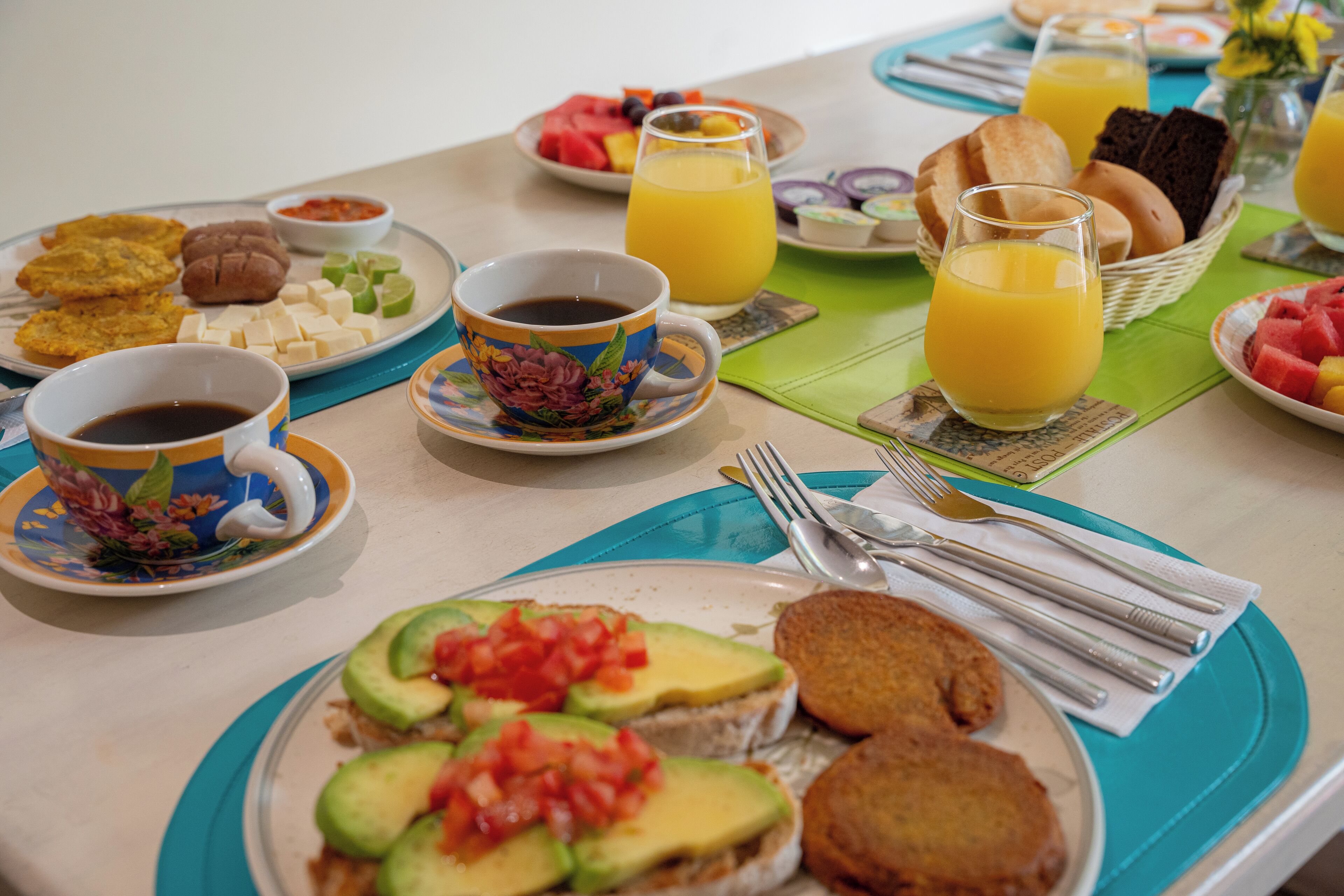 A breakfast table with various food items, including toast with avocado, fruit, and beverages.
