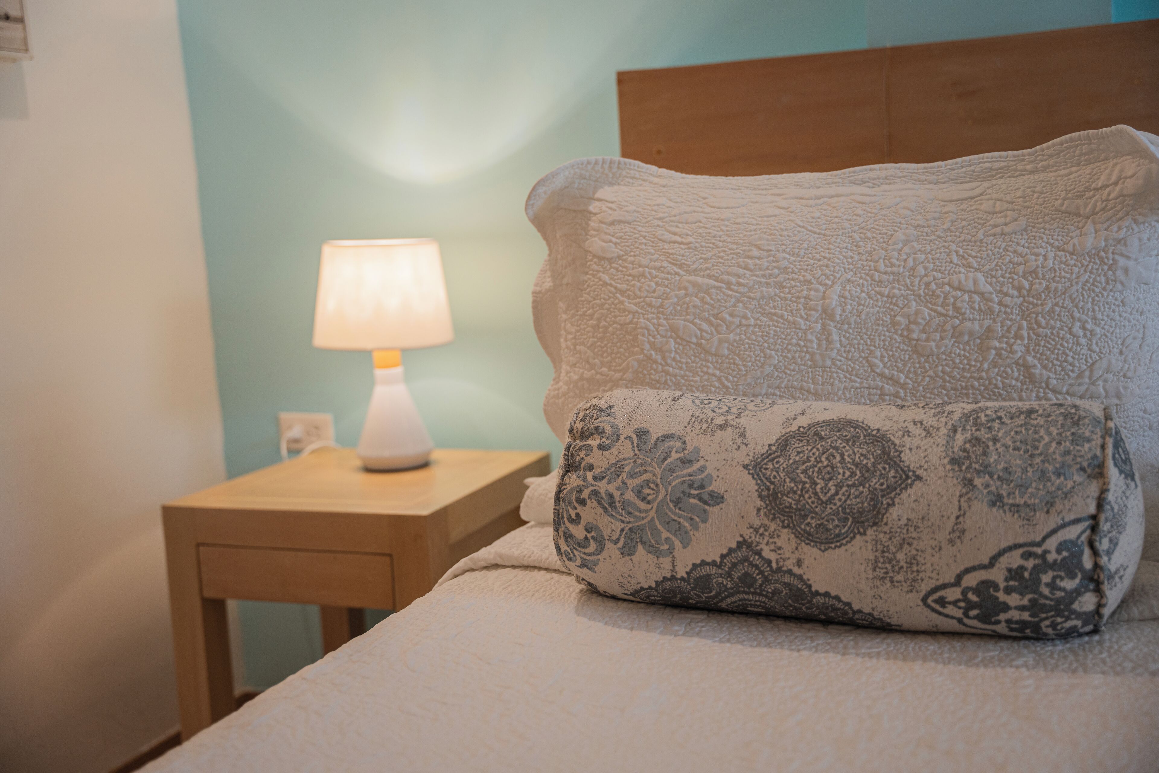 A neatly made bed with a patterned pillow and a bedside table with a lamp.