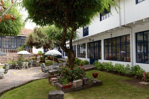 A courtyard with outdoor seating, a tree, and a building with large windows. - La Casa De Fray Bartolome (Cusco)