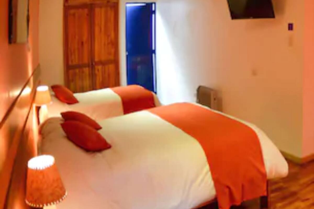 Ein Schlafzimmer mit zwei Betten, Holzbalken an der Decke, einem Fernseher an der Wand und einer Tür im Hintergrund.