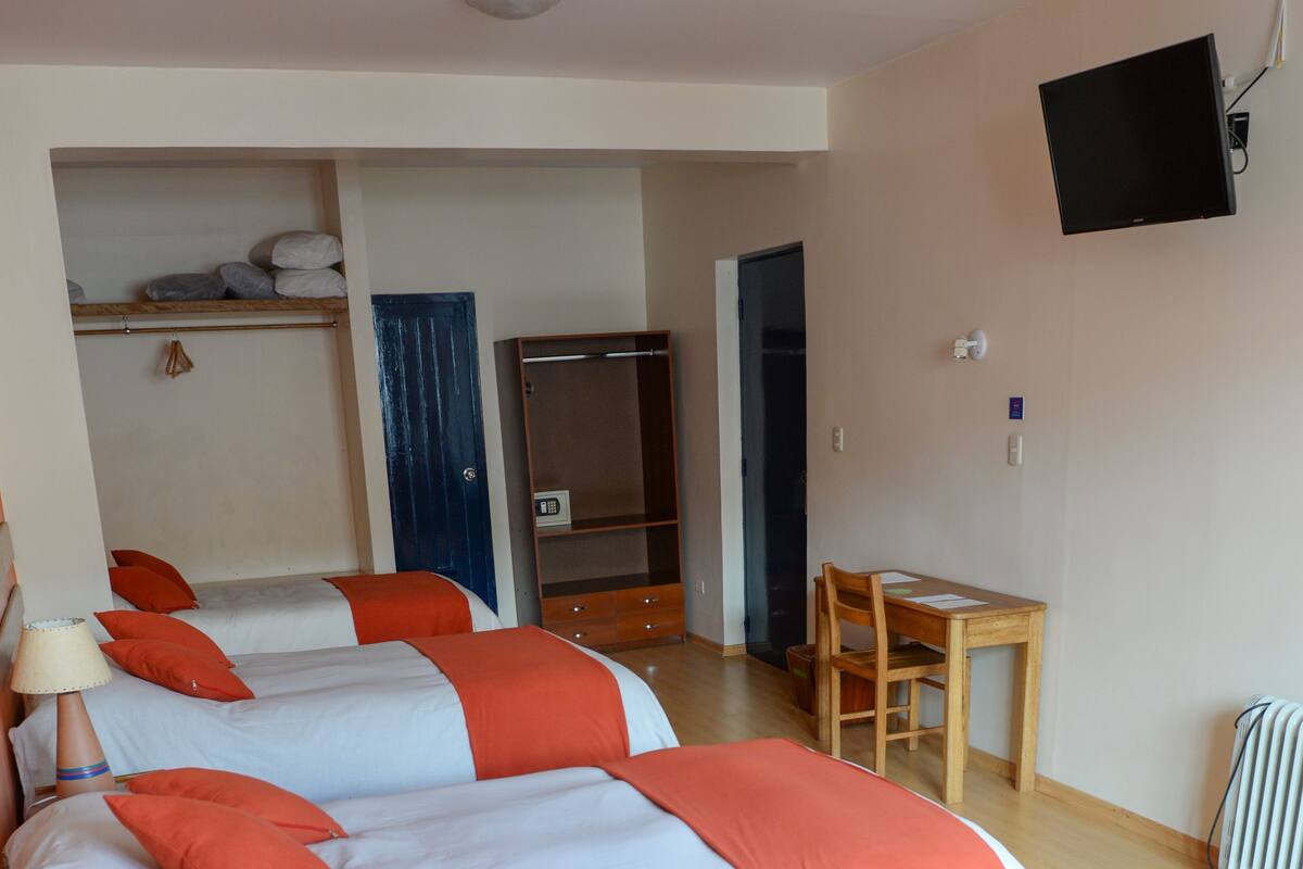 Ein Hotelzimmer mit drei Betten, einem Schreibtisch und einem Fernseher.