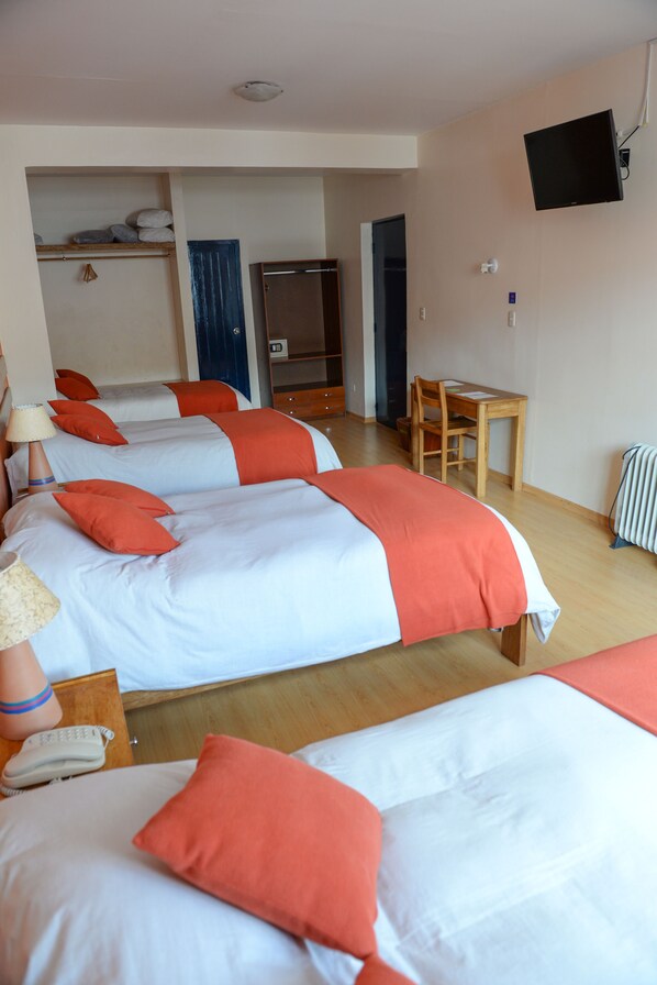 A hotel room with three beds, a desk, and a television.