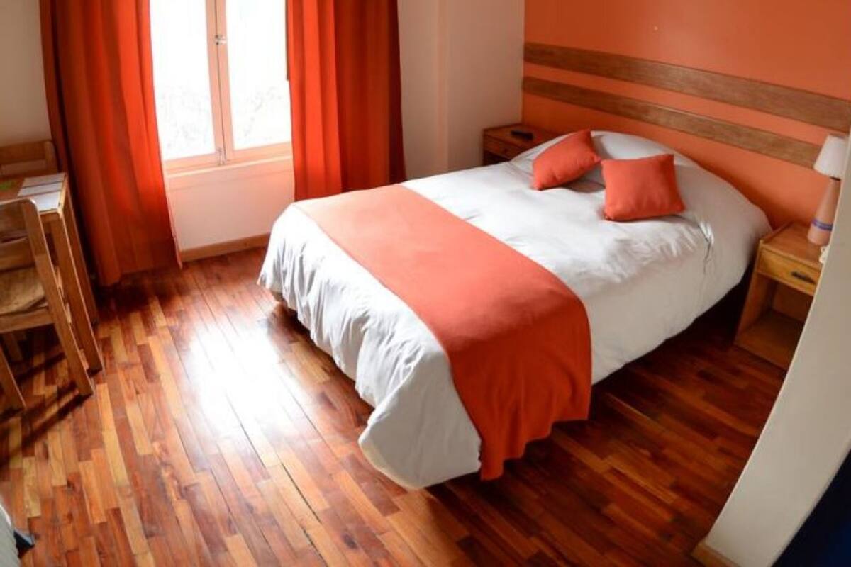Ein Schlafzimmer mit einem Bett, Holzboden, orangefarbenen Vorhängen und einem Fenster.