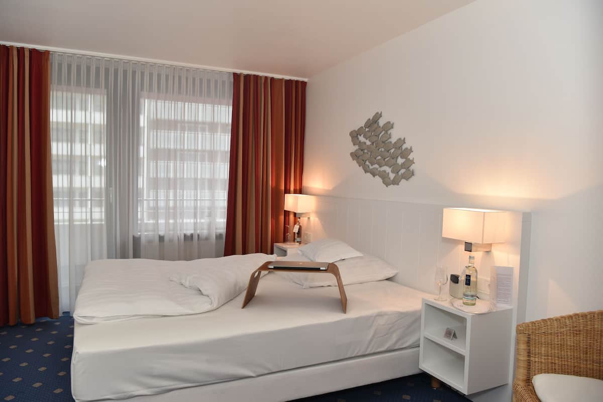 A hotel room with a bed, a nightstand, a lamp, a bottle, and a decorative wall piece.