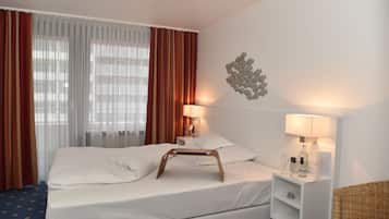 A hotel room with a bed, a nightstand, a lamp, a bottle, and a decorative wall piece.