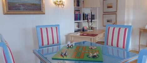 A room with a glass-top table, striped chairs, a bookshelf, a lamp, and a framed painting.