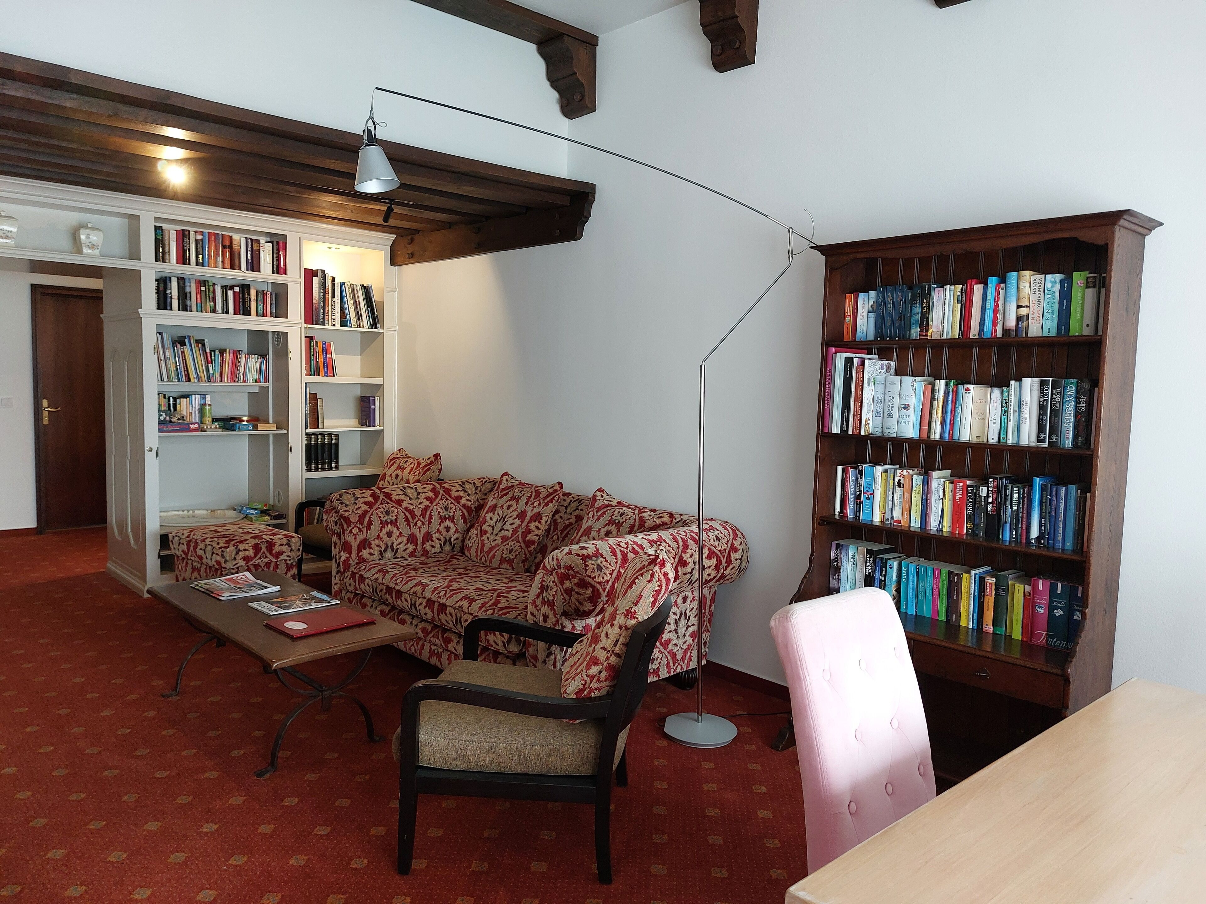 Een gezellige woonkamer met een bloemenbank, een houten salontafel en een boekenkast vol boeken.