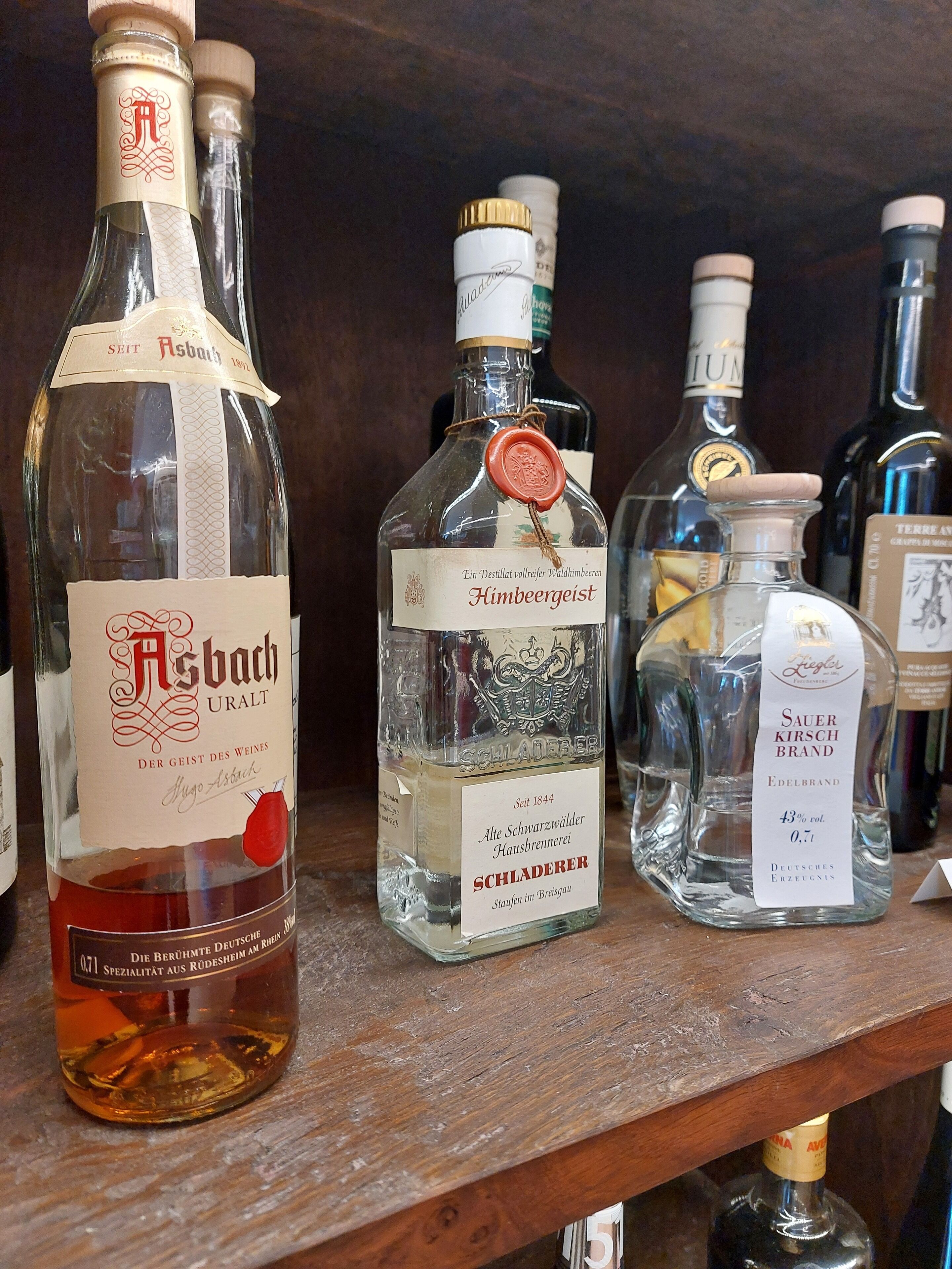 A shelf with various bottles of alcohol, including a prominent bottle labeled "Asbach URALT" and another labeled "Schlagerer."