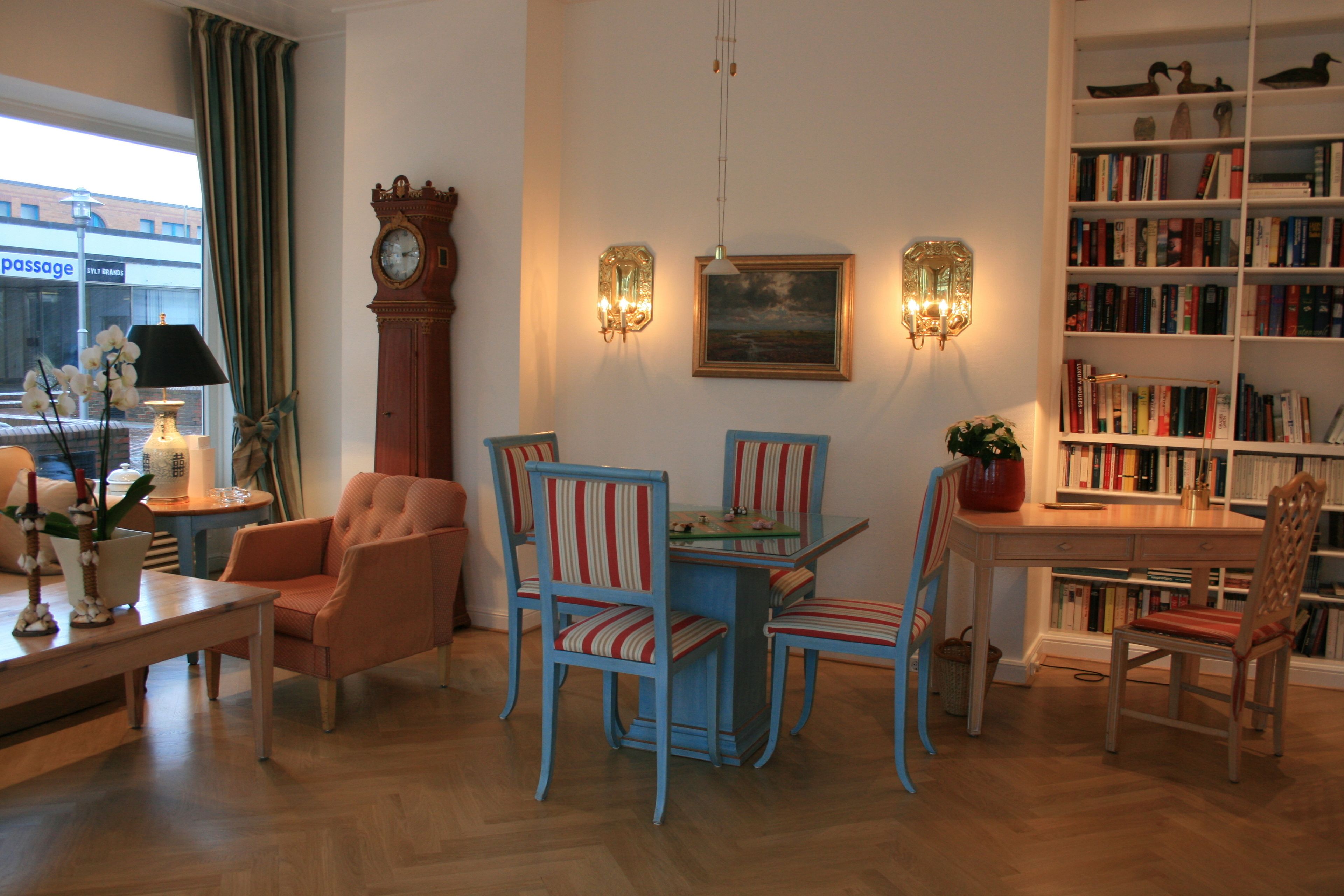 A cozy living room with a wooden coffee table, striped chairs, a bookshelf, and a large clock.