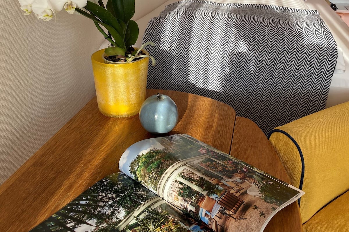 A neatly arranged hotel room with a bed, a bedside table with a vase of white orchids, a decorative wall piece, and a magazine.