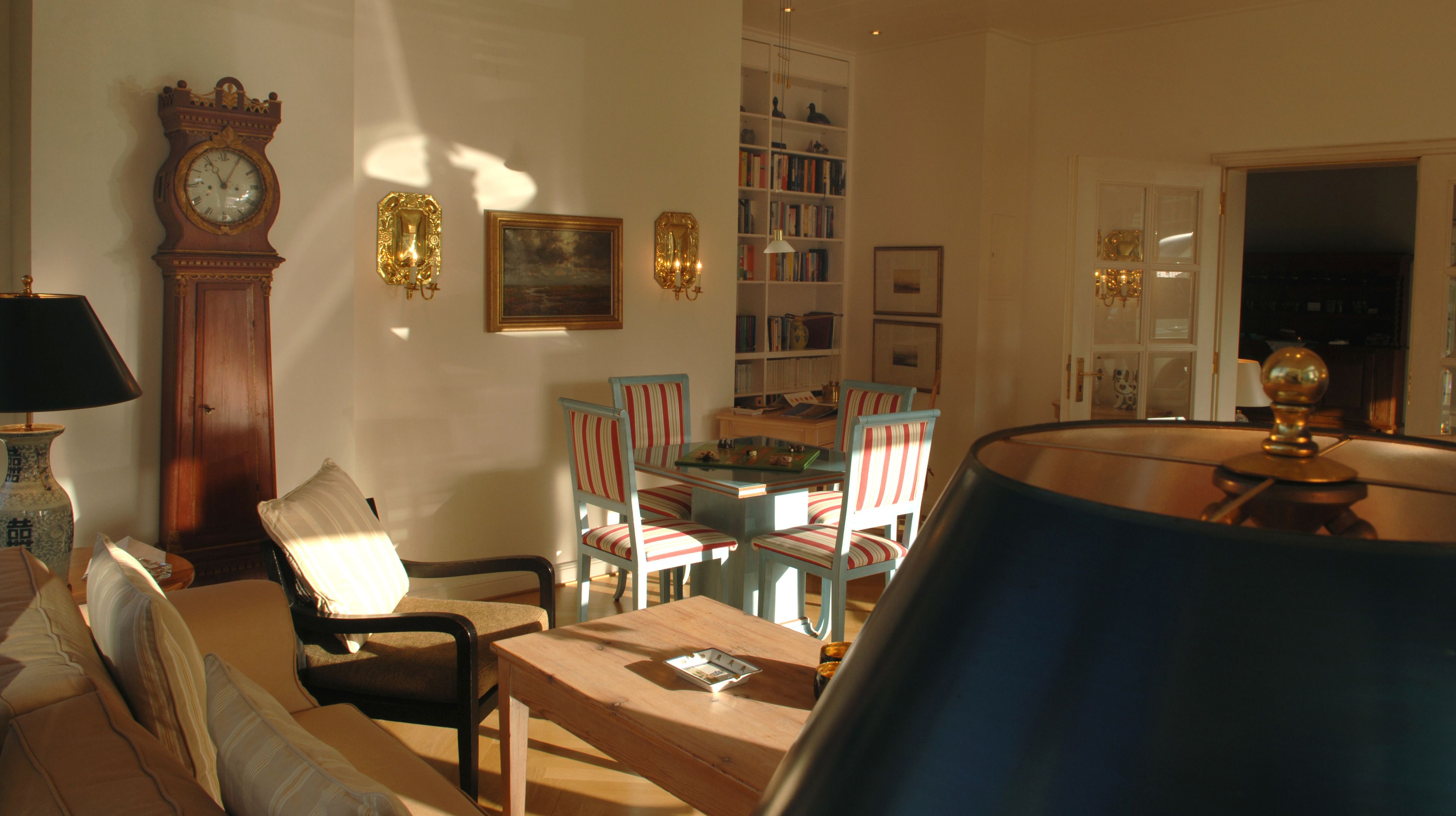 A living room with a sofa, armchairs, a coffee table, a bookshelf, a clock, and a lamp.