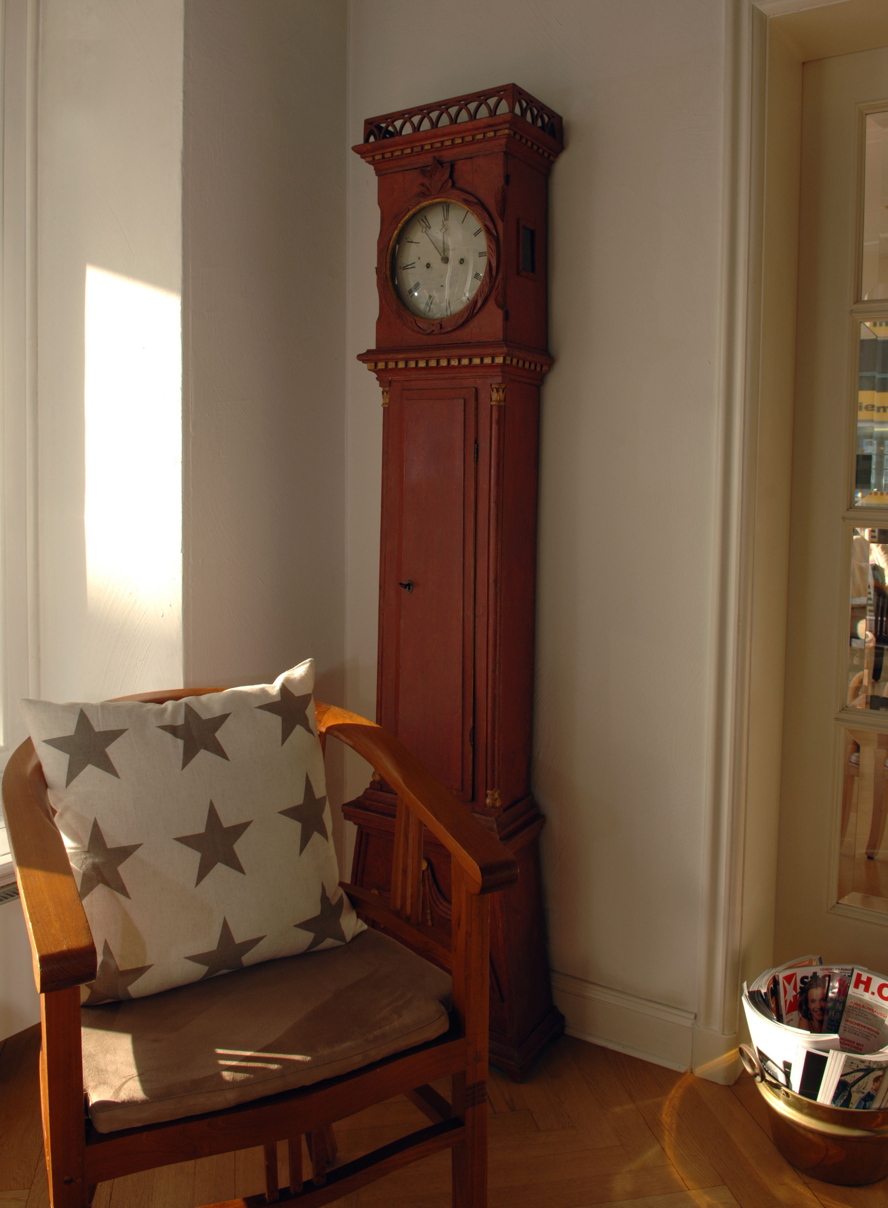 A wooden chair with a cushion featuring star patterns, positioned next to a tall wooden grandfather clock.