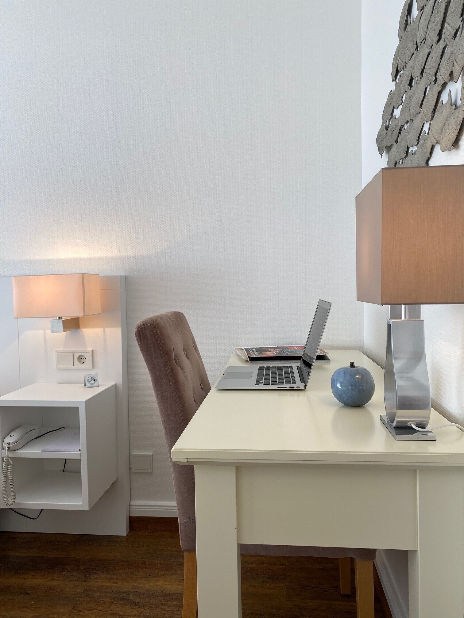 Une pièce moderne avec un bureau blanc, un ordinateur portable, une pomme bleue, une lampe et un téléphone.
