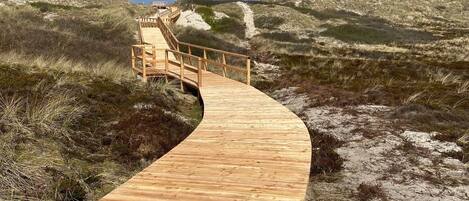 A wooden boardwalk leading to a beach area with dunes and a clear sky.