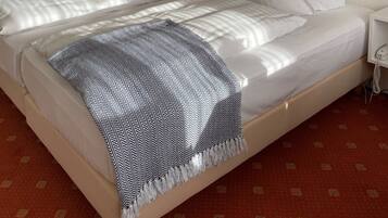 Ein Hotelzimmer mit einem großen Bett, weißer Bettwäsche, einer gemusterten Tagesdecke, einem Nachttisch mit einer Lampe und einem Bild an der Wand.