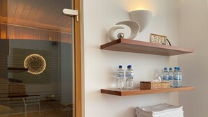 A hotel room with wooden shelves displaying water bottles, a framed picture, and a stack of towels. - Hotel Wünschmann (Sylt)