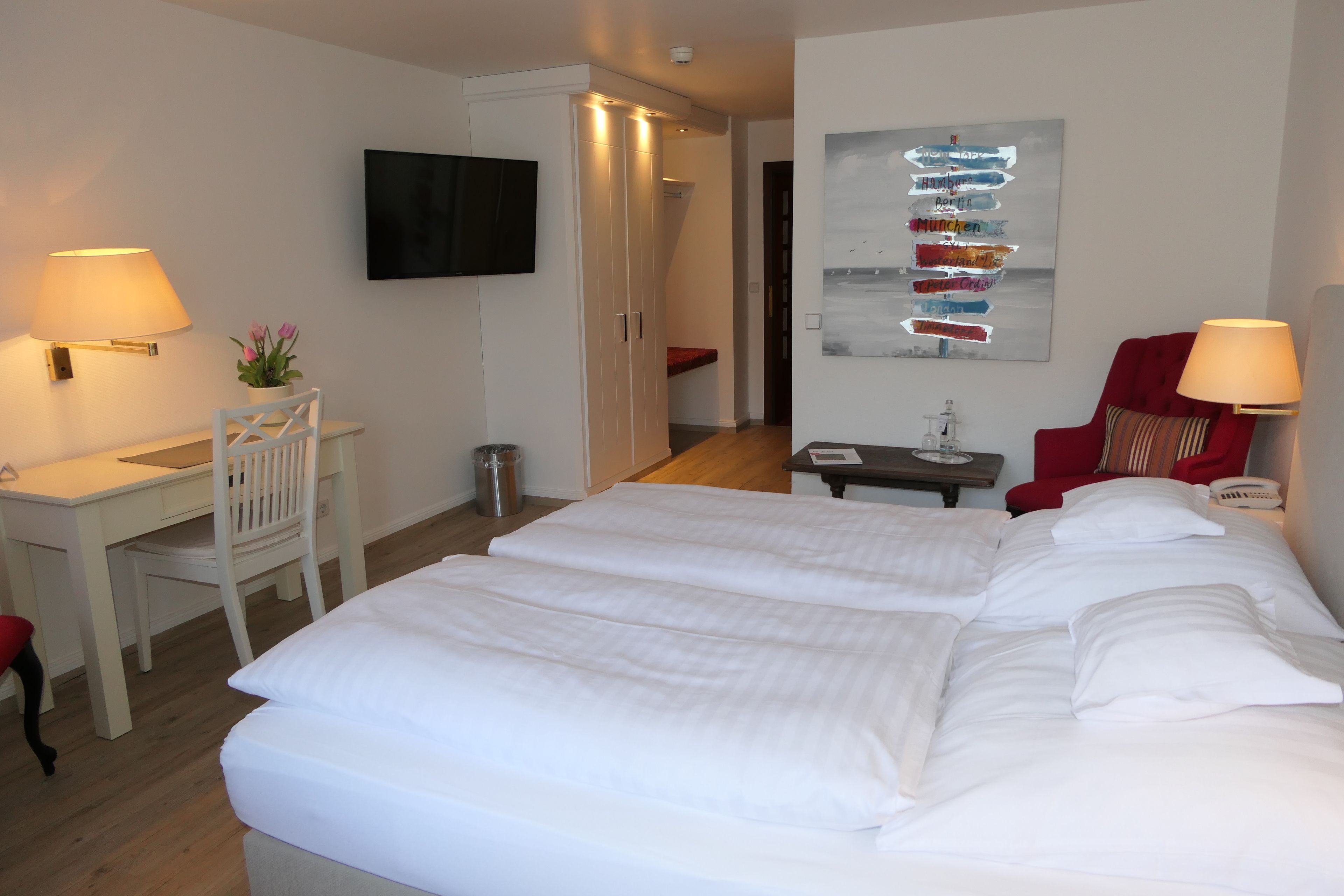A hotel room with a large bed, a desk, a chair, a TV, and a wall art piece.