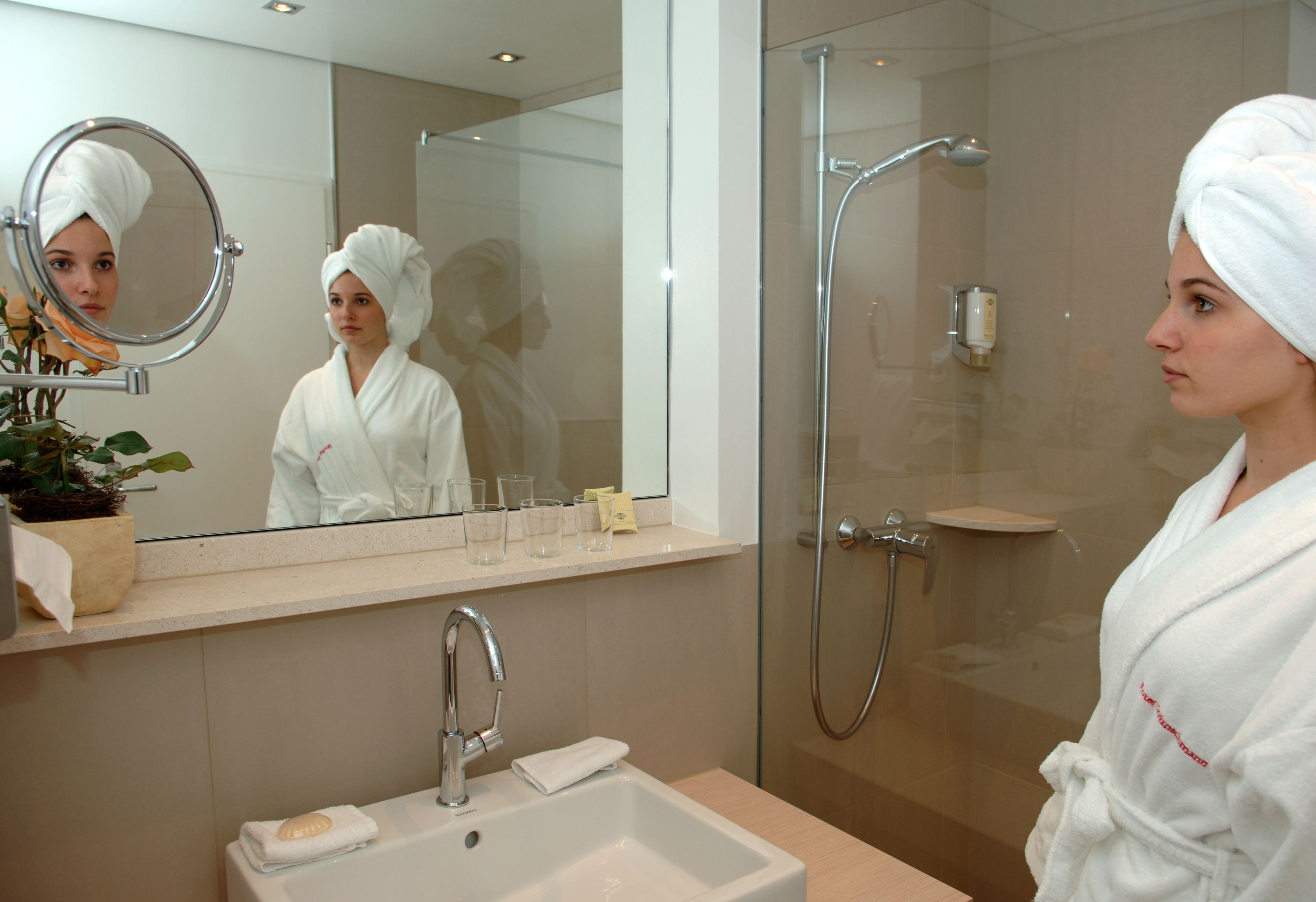 A modern bathroom with a glass-enclosed shower, a sink with a soap dish, and a mirror with a round frame.