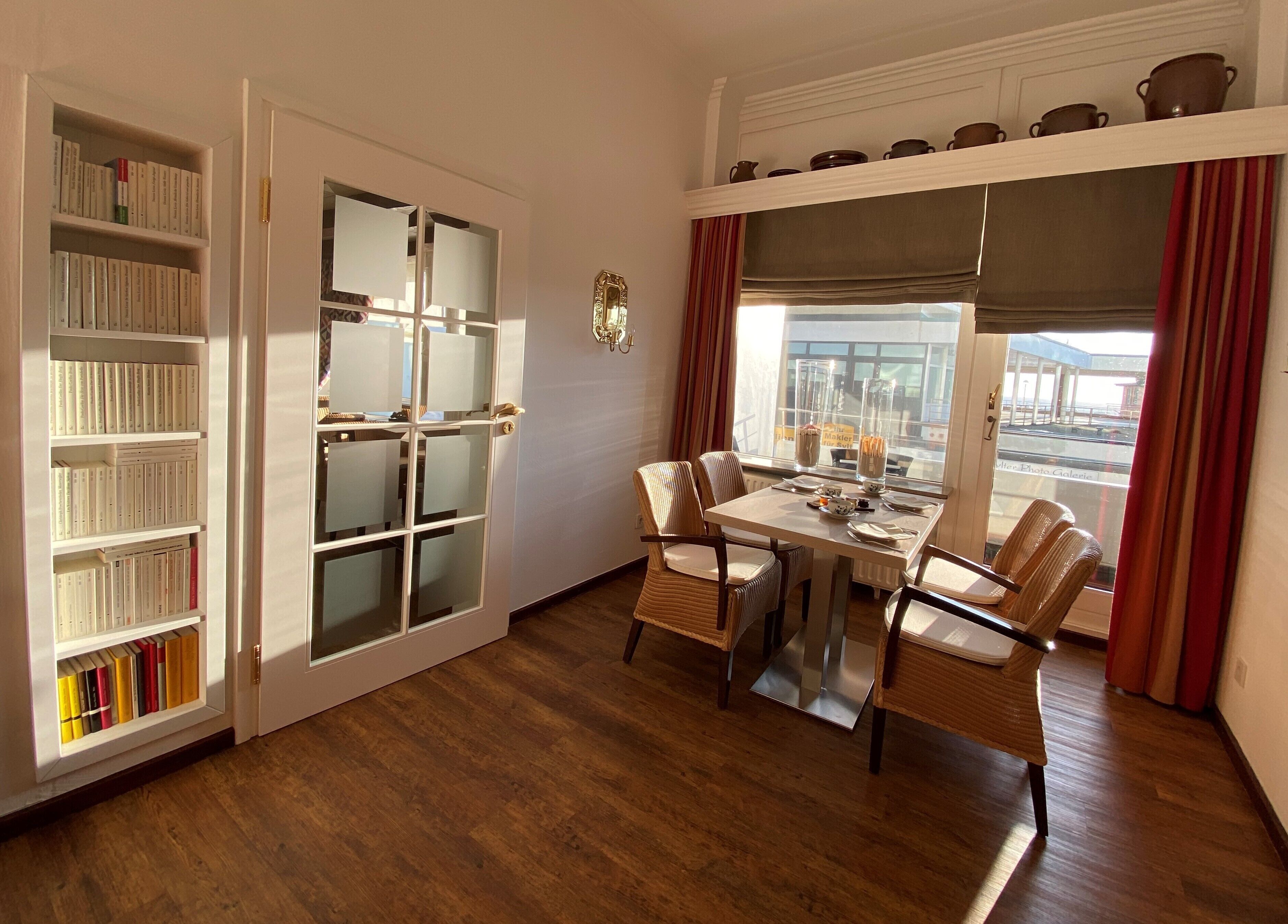 A room with a dining table, chairs, a bookshelf, and a window with curtains.